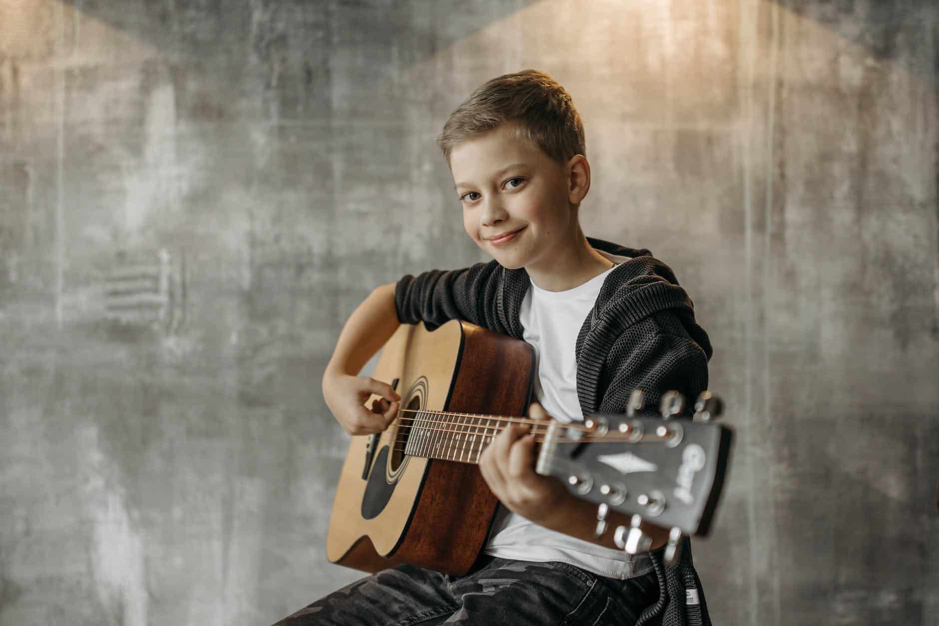 a young boy smiling while holding a guitar